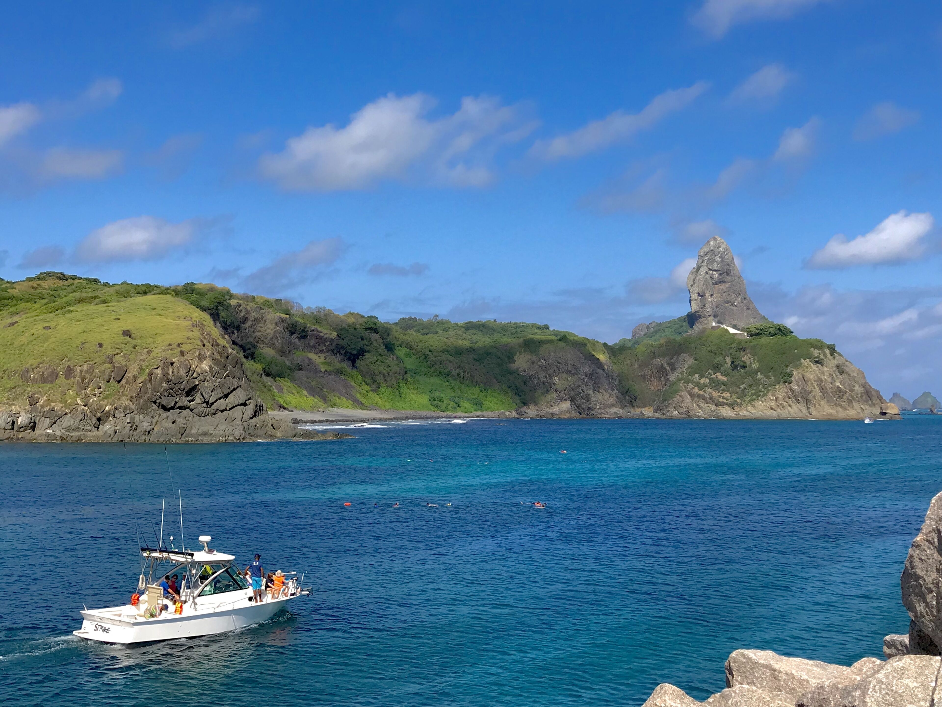 A boat on a clear blue sea with rocky hills in the background.