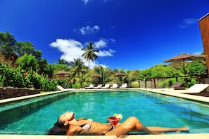 A pool area with a person lying on the edge, lounge chairs, and umbrellas. - Pousada do Vale (Fernando de Noronha)