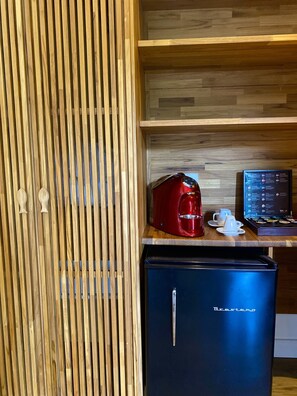 A compact kitchenette with a red coffee maker, a small refrigerator, and a wooden panel wall. - Pousada do Vale (Fernando de Noronha)