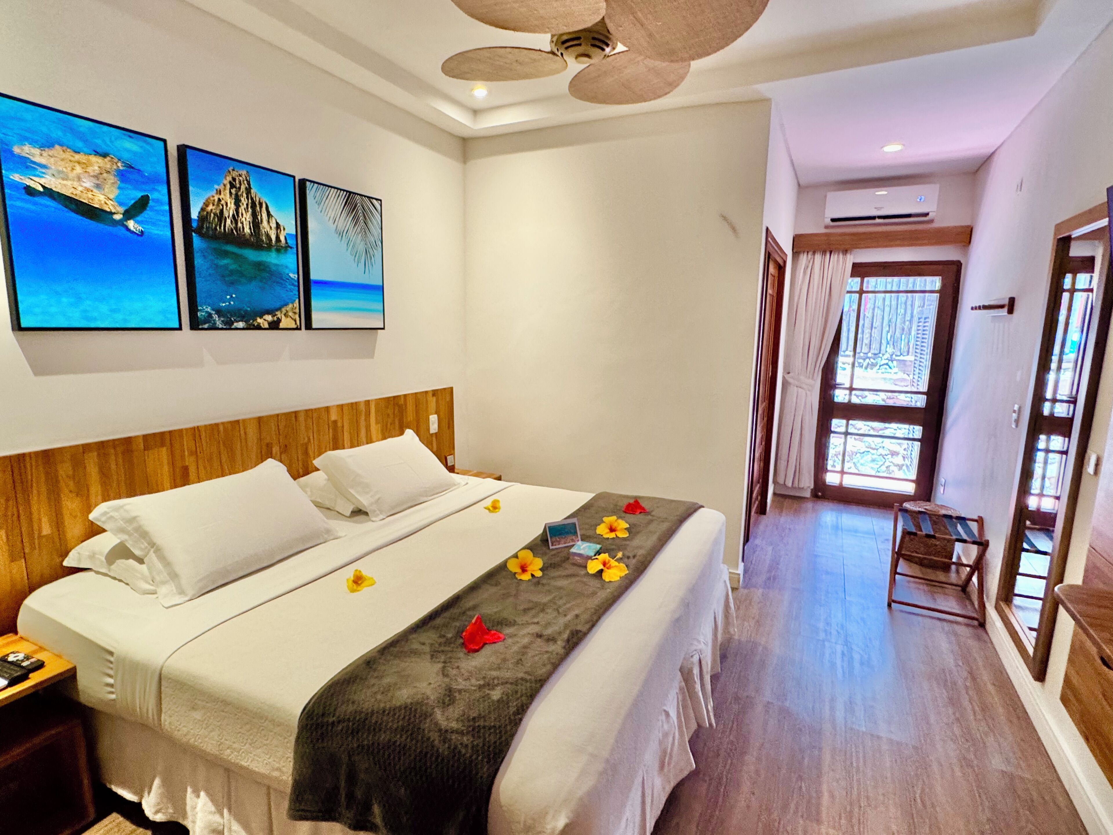 A hotel room with a bed, a wooden headboard, a ceiling fan, and wall art depicting a beach scene.