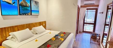 A hotel room with a bed, a wooden headboard, a ceiling fan, and wall art depicting a beach scene.