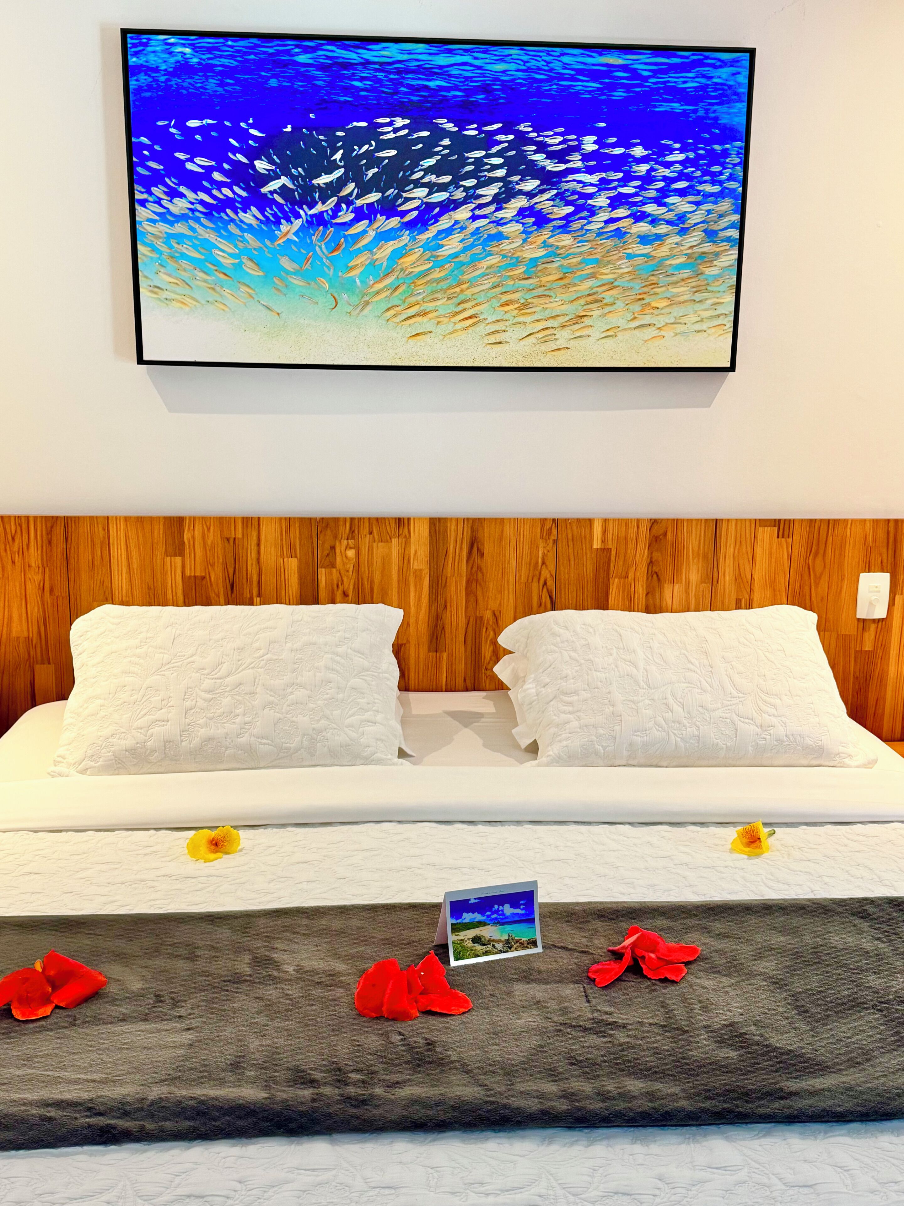 Una cama bien hecha con sábanas blancas, cabecera de madera y un cuadro enmarcado sobre la cama.