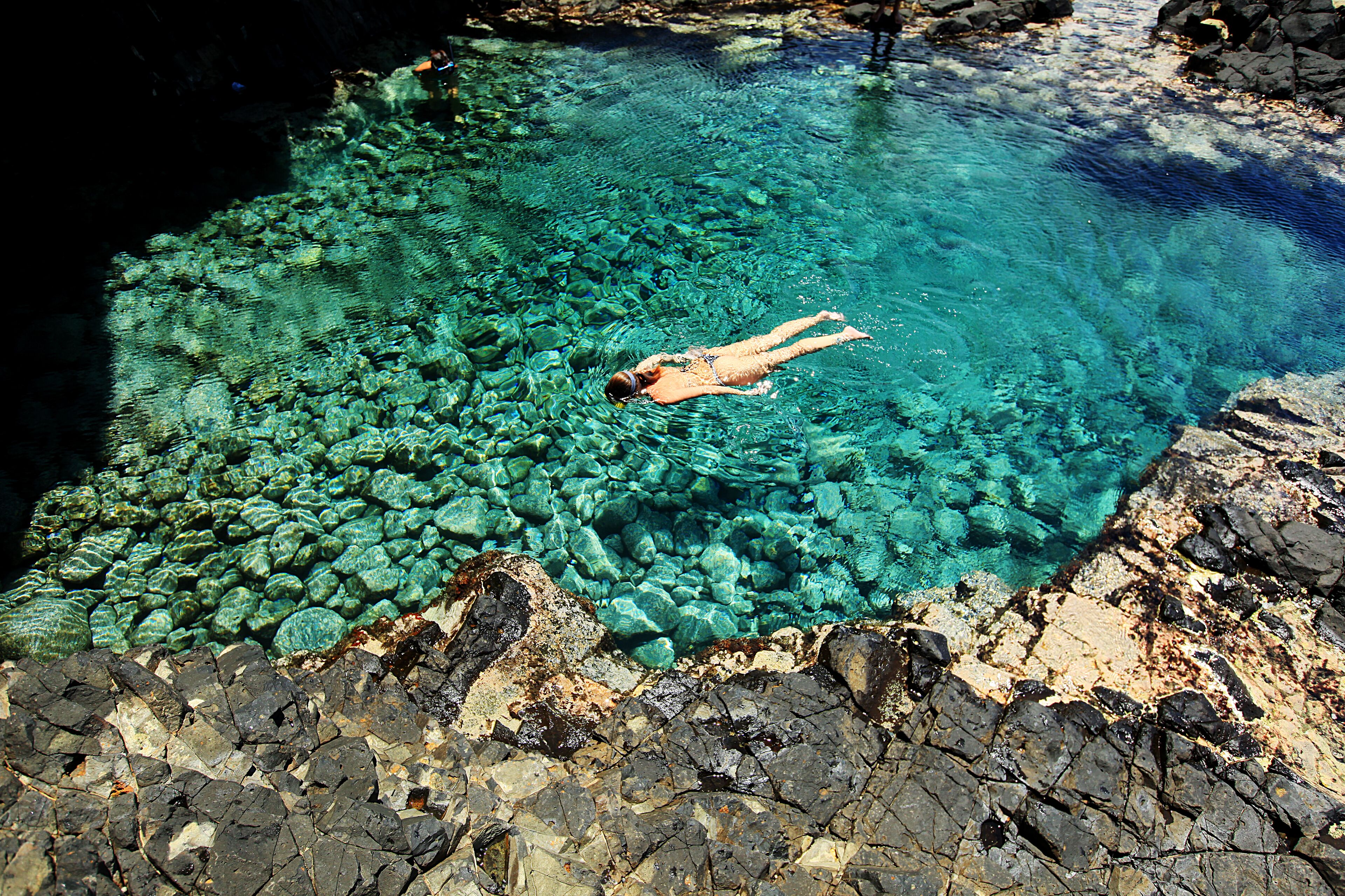 A person swimming in a clear pool surrounded by rocky terrain.