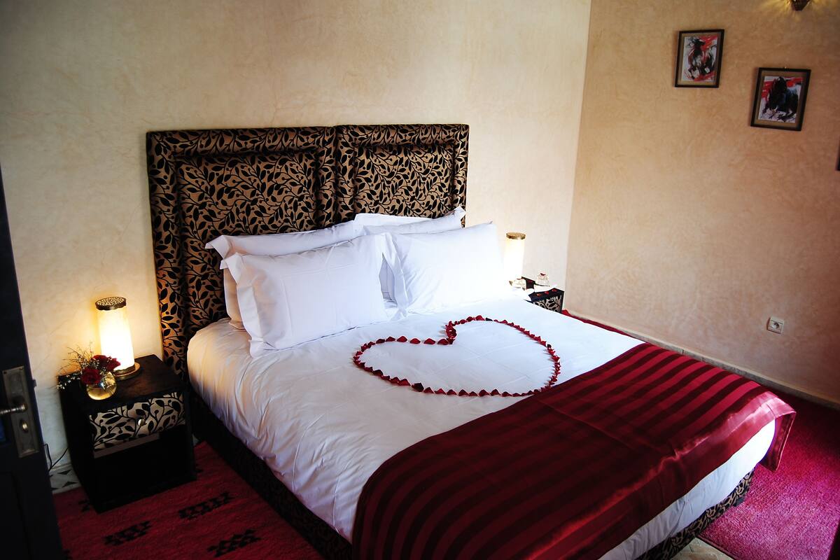 A bed with a heart-shaped decoration, a patterned headboard, and a red blanket.