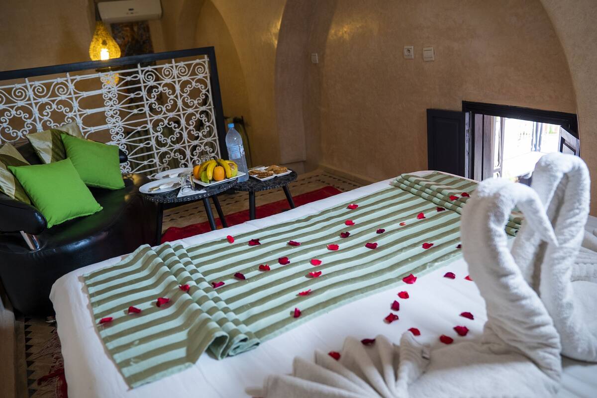 A hotel room with a bed, a sofa, a small table with fruits, and a decorative headboard.