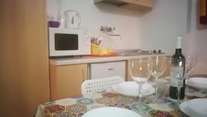 Une petite cuisine équipée d’un four à micro-ondes, d’une bouilloire et d’un évier. Il y a deux verres à vin et une bouteille sur la table.