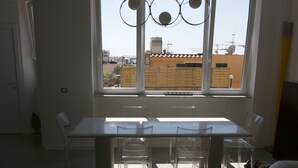 A modern dining area with a large table and chairs, a view of buildings through a window, and a ceiling light fixture. - Casa Maria (Salerno)