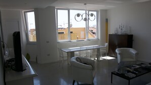A modern living room with a white sofa, a coffee table, and a dining area with a table and chairs. - Casa Maria (Salerno)