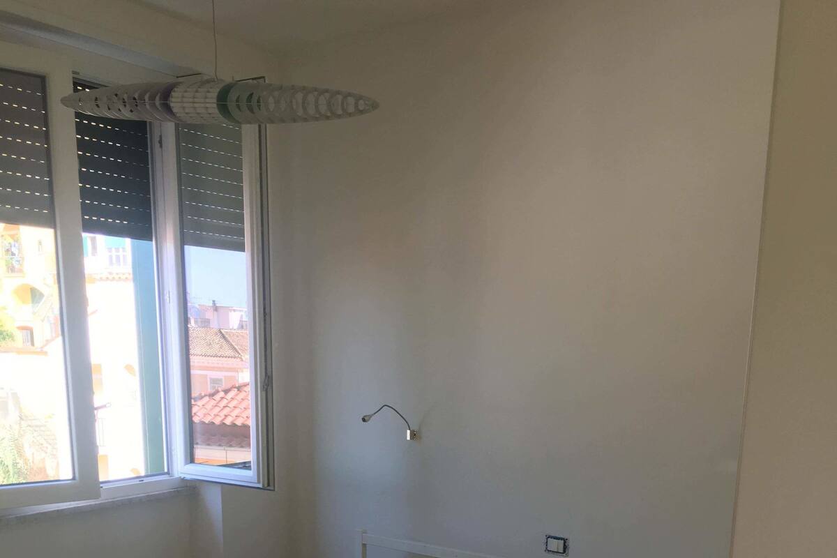 A room with a bed, a window with blinds, and a wall-mounted light fixture.