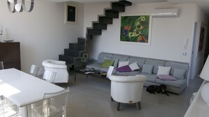 A modern living room with a staircase, a dining area with a white table and chairs, and a grey sofa with cushions. - Casa Maria (Salerno)