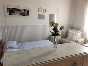A hotel room with a bed, a bedside table with a vase of flowers, a chair, a radiator, and a framed picture on the wall. - Casa Maria (Salerno)