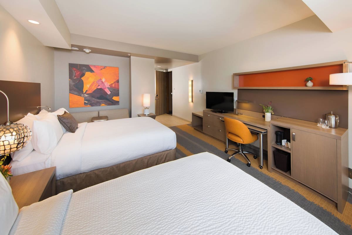 Una habitación de hotel con dos camas, un escritorio, un televisor y una planta pequeña.