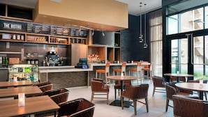 A modern bistro with a bar area, seating, and a large window offering a view of the city. - Courtyard Phoenix Downtown (Phoenix)