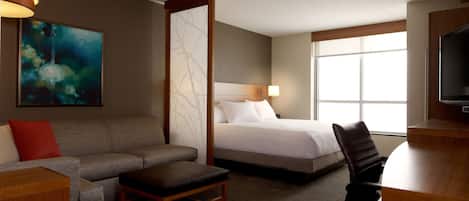 A hotel room with a bed, a sofa, a desk, a chair, a TV, and a window.