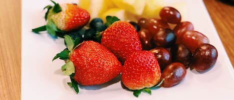 Un plato blanco con fresas, arándanos y uvas sobre una mesa de madera.