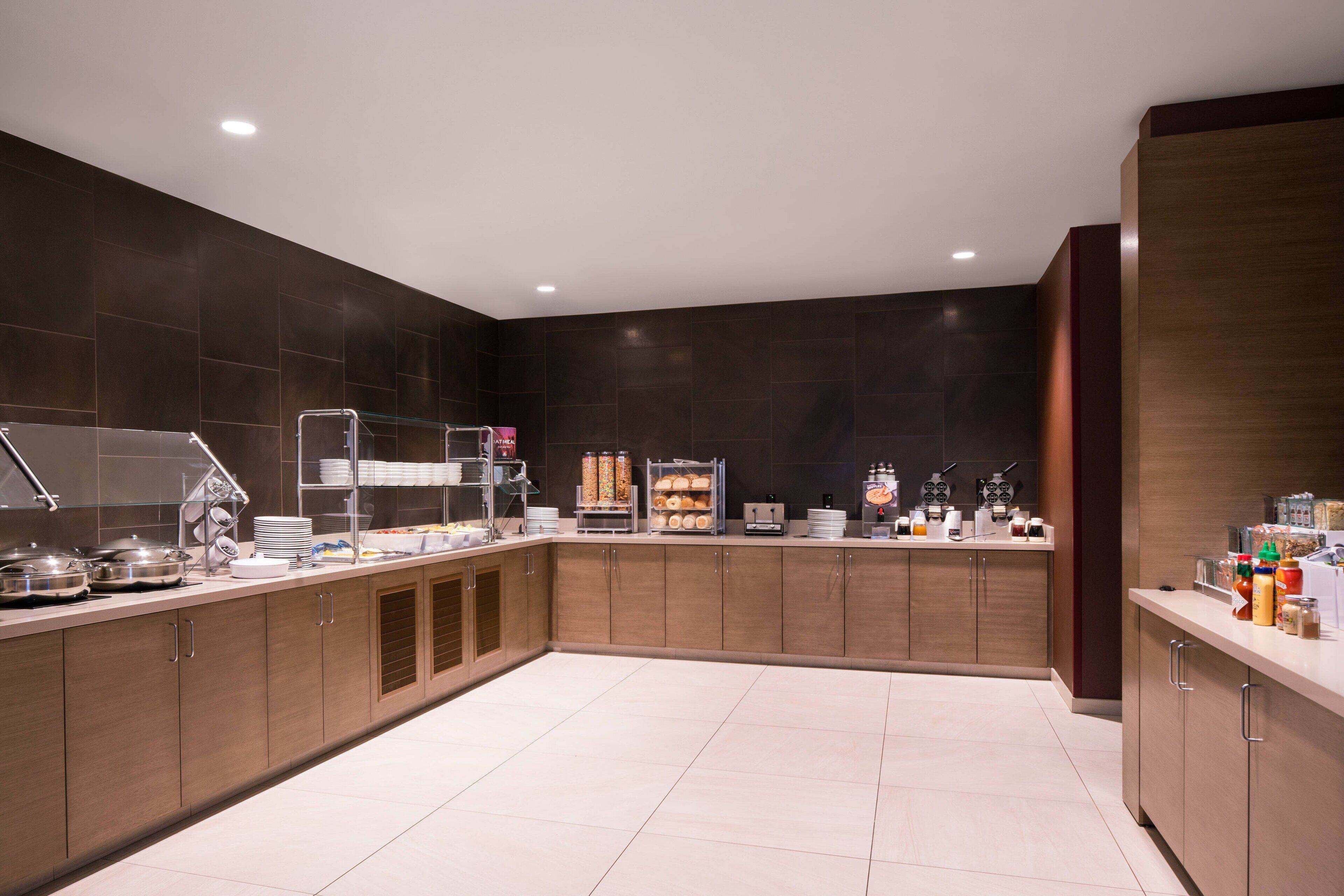 A modern kitchen with dark tiled walls, wooden cabinets, and a clean, tiled floor.