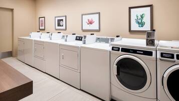 A laundry facility with multiple washing machines and dryers, a wooden bench, and framed artwork on the walls.