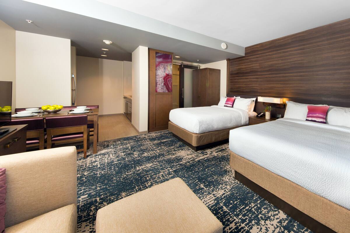 A hotel room with a bed, a desk, a chair, and a small table with a bowl of fruit.
