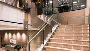 Un intérieur moderne agrémenté d’un escalier, de rampes en verre et d’un luminaire contemporain.
