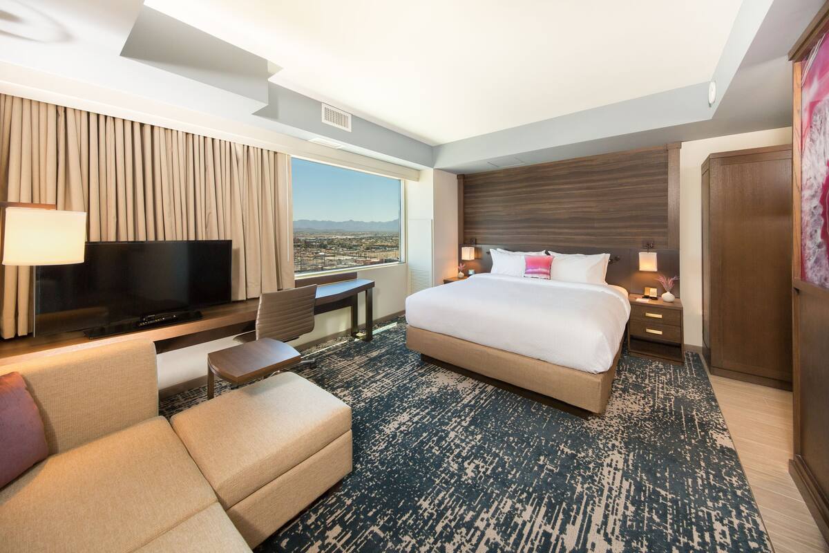 A modern hotel room with a large bed, a flat-screen TV, a desk, and a view of the city.