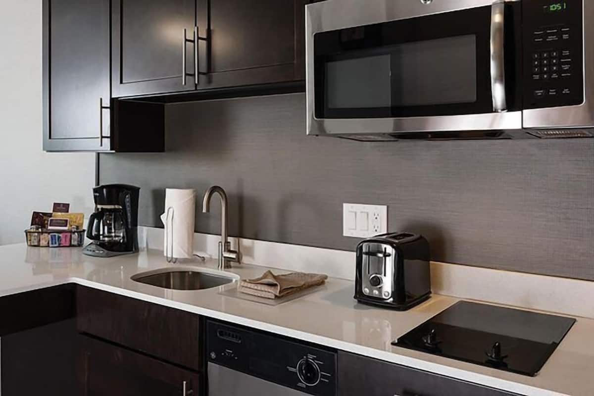 A modern kitchen with dark cabinets, a stainless steel microwave, a coffee maker, a toaster, and a dishwasher.