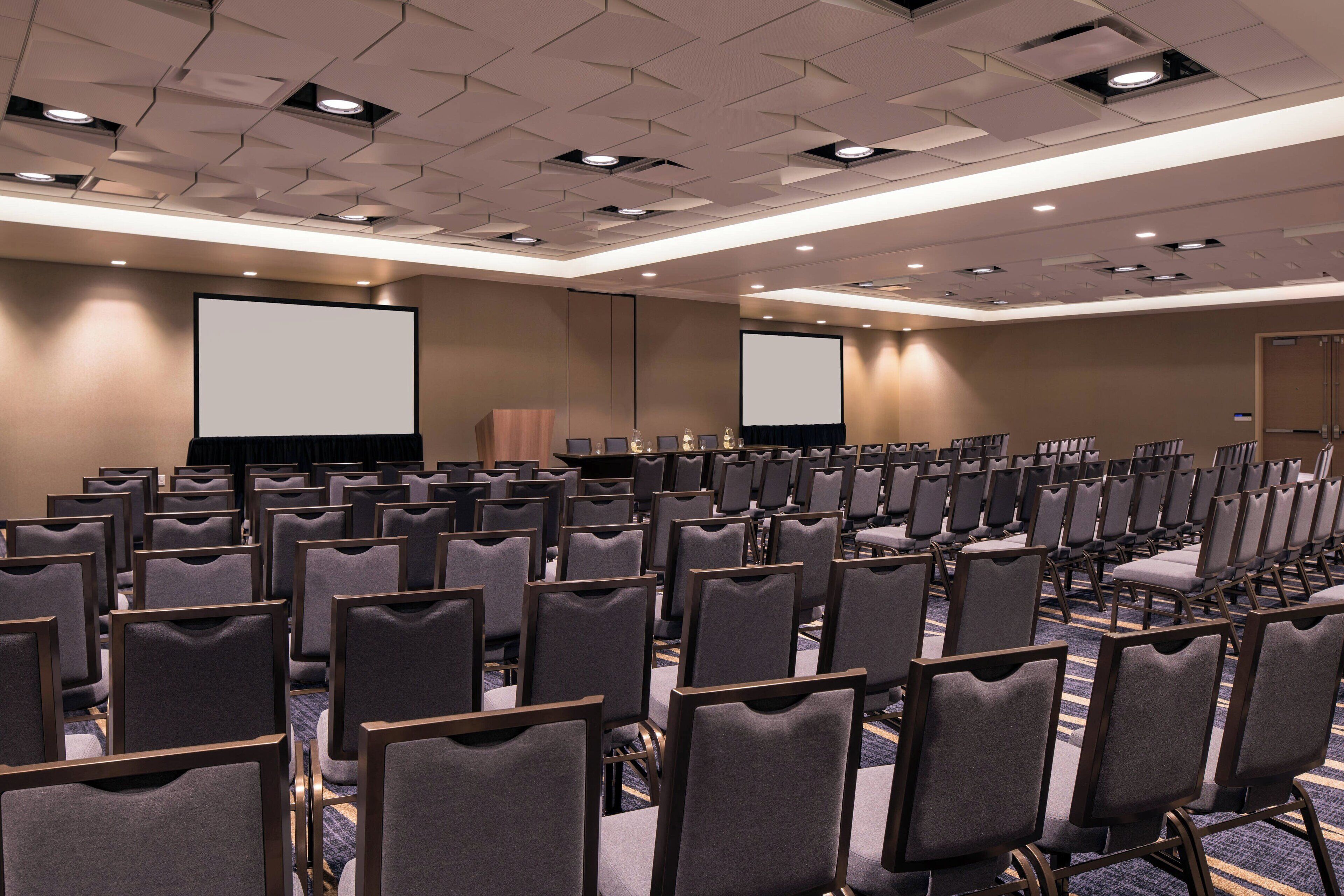 A conference room with rows of chairs, a large screen, and a podium.