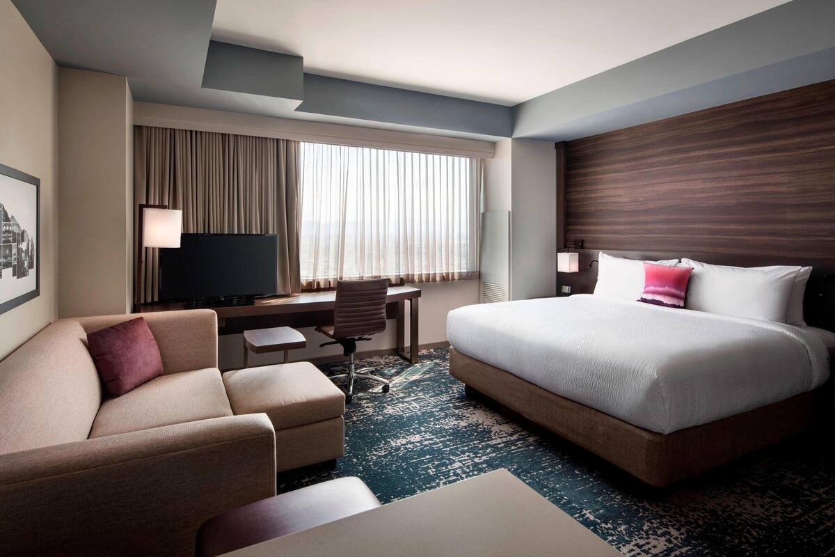 A hotel room with a bed, a desk, a chair, and a television.