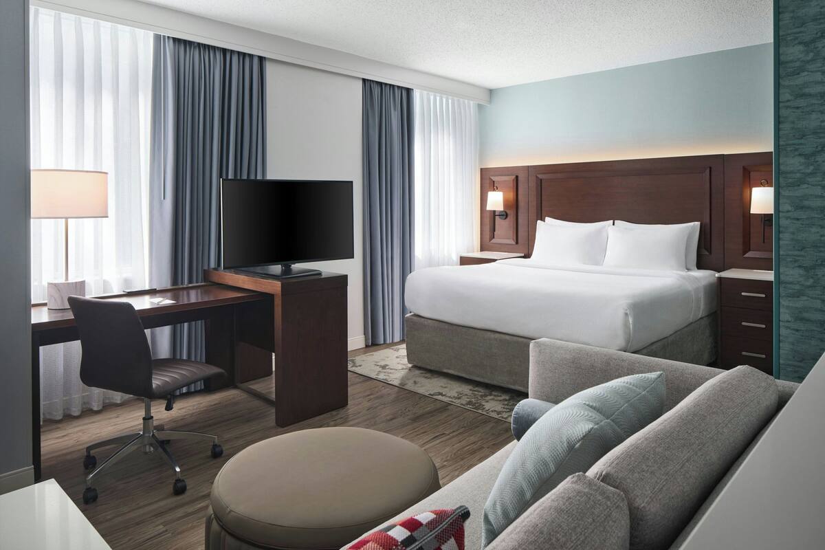 Ein Hotelzimmer mit einem Bett, einem Schreibtisch mit Stuhl, einem Fernseher und einem Sofa.
