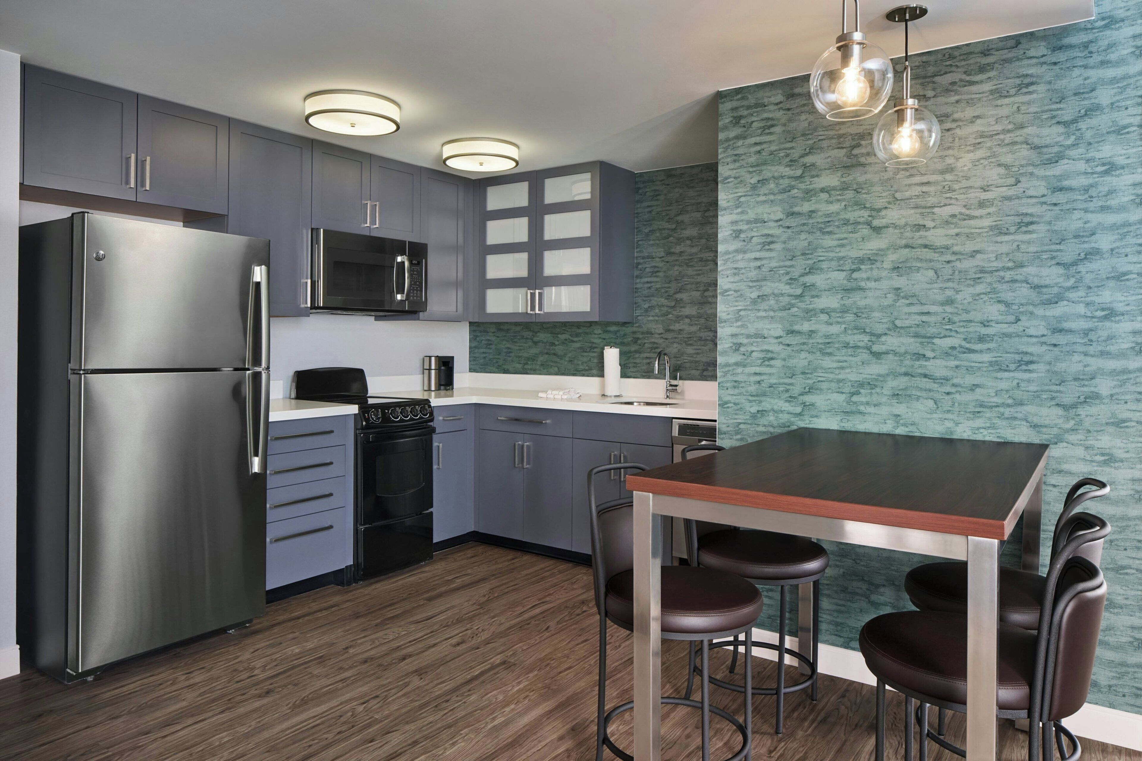 A modern kitchen with grey cabinets, stainless steel appliances, a wooden dining table, and bar stools.