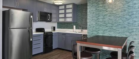 A modern kitchen with grey cabinets, stainless steel appliances, a wooden dining table, and bar stools.