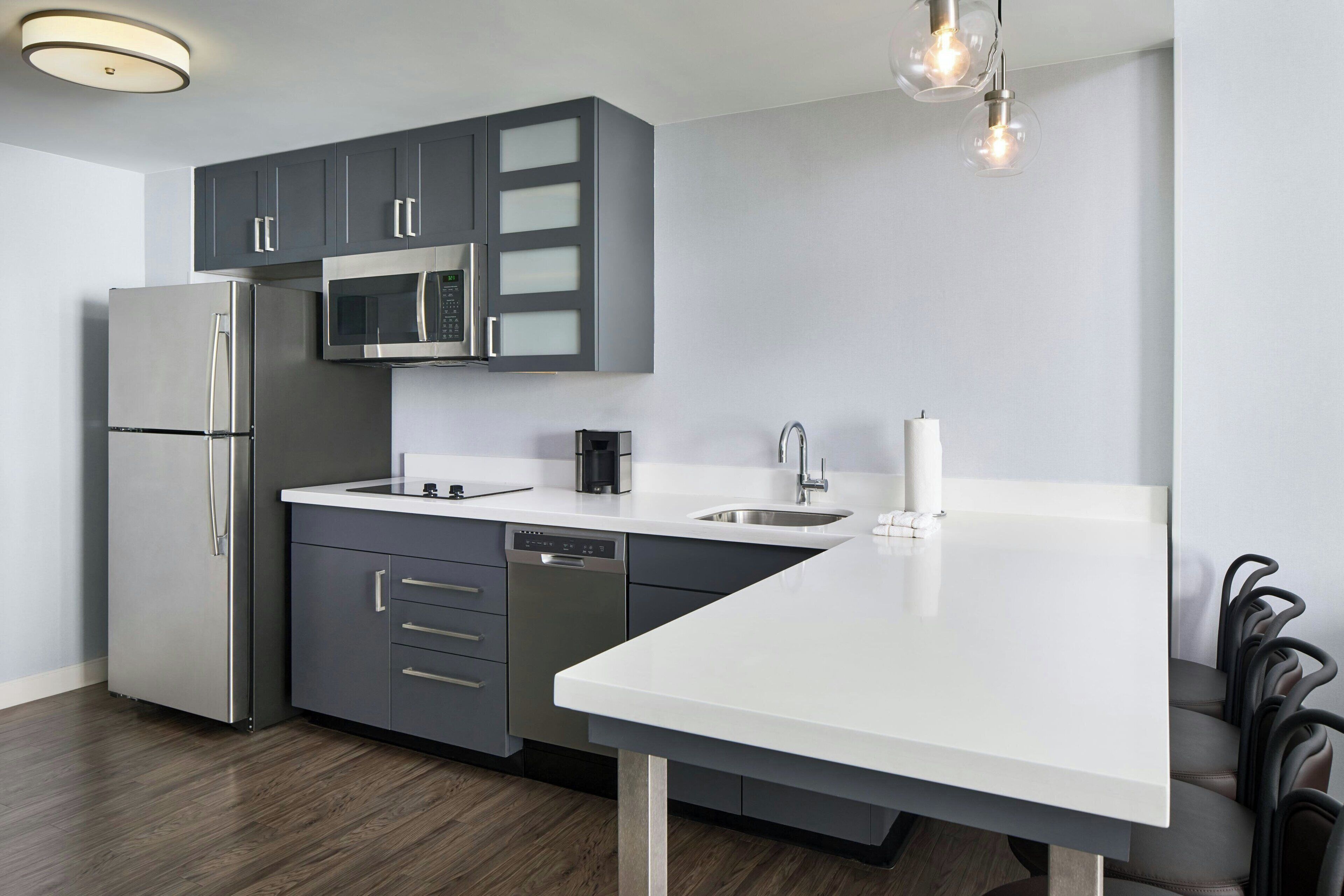 A modern kitchen with grey cabinets, stainless steel appliances, a white countertop, and a built-in dishwasher.