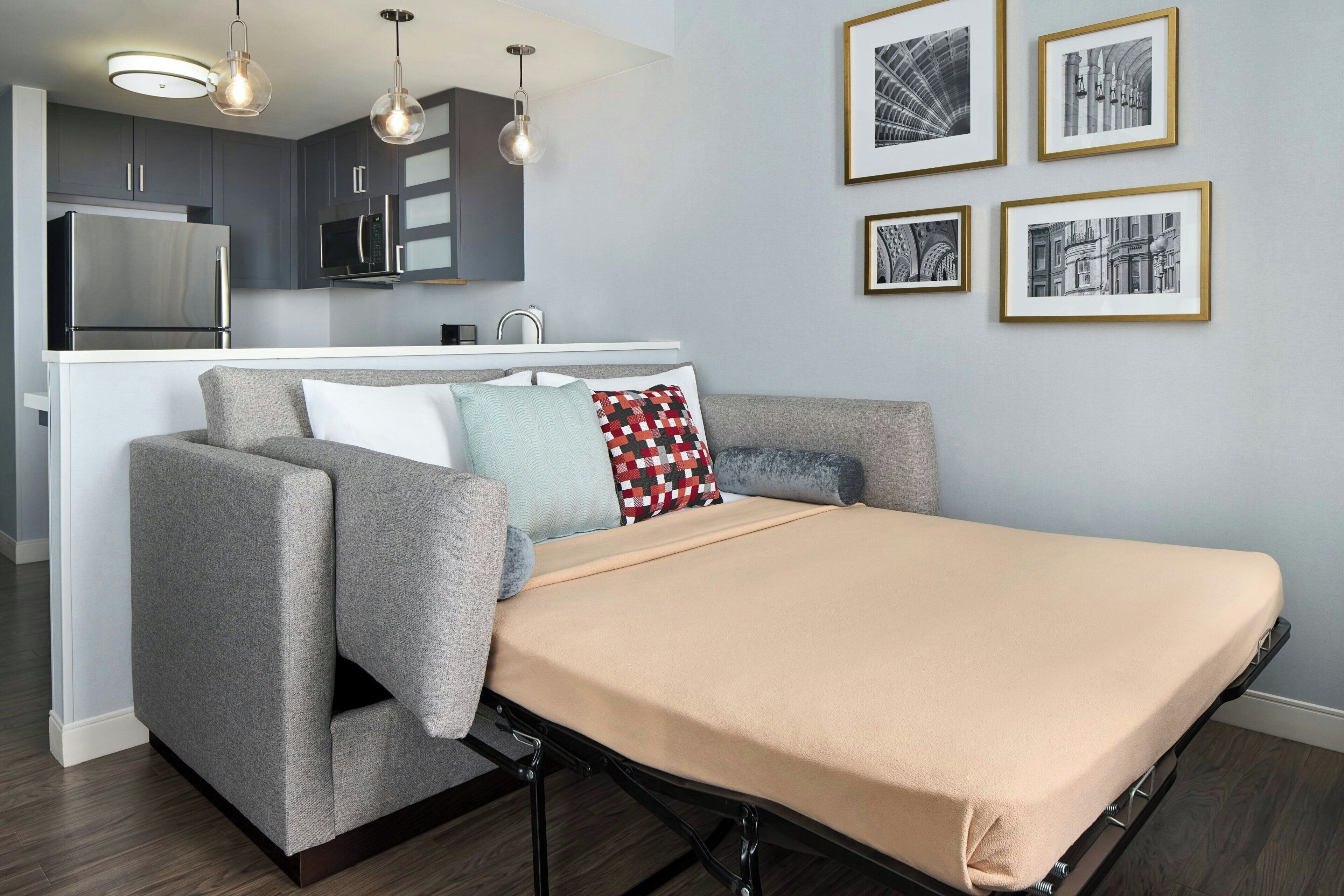 Un espace de vie moderne comprenant un canapé, un lit, un coin cuisine et des tableaux encadrés accrochés au mur.