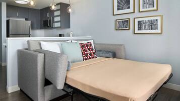 A modern living space with a sofa, a bed, a kitchen area, and framed pictures on the wall.