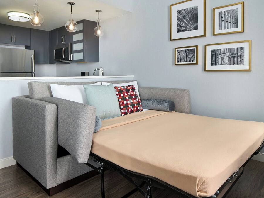 A modern living space with a sofa, a bed, a kitchen area, and framed pictures on the wall.
