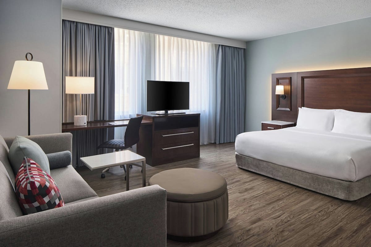 Ein Hotelzimmer mit einem Bett, einem Schreibtisch mit Fernseher, einem Sessel, einer Lampe und einem Sofa.