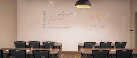 A conference room with tables, chairs, and a whiteboard with mathematical equations and graphs.