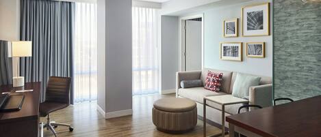 Una habitación de hotel moderna con suelo de madera, un escritorio con lámpara, un sofá, una mesita de centro y cuadros enmarcados en la pared.