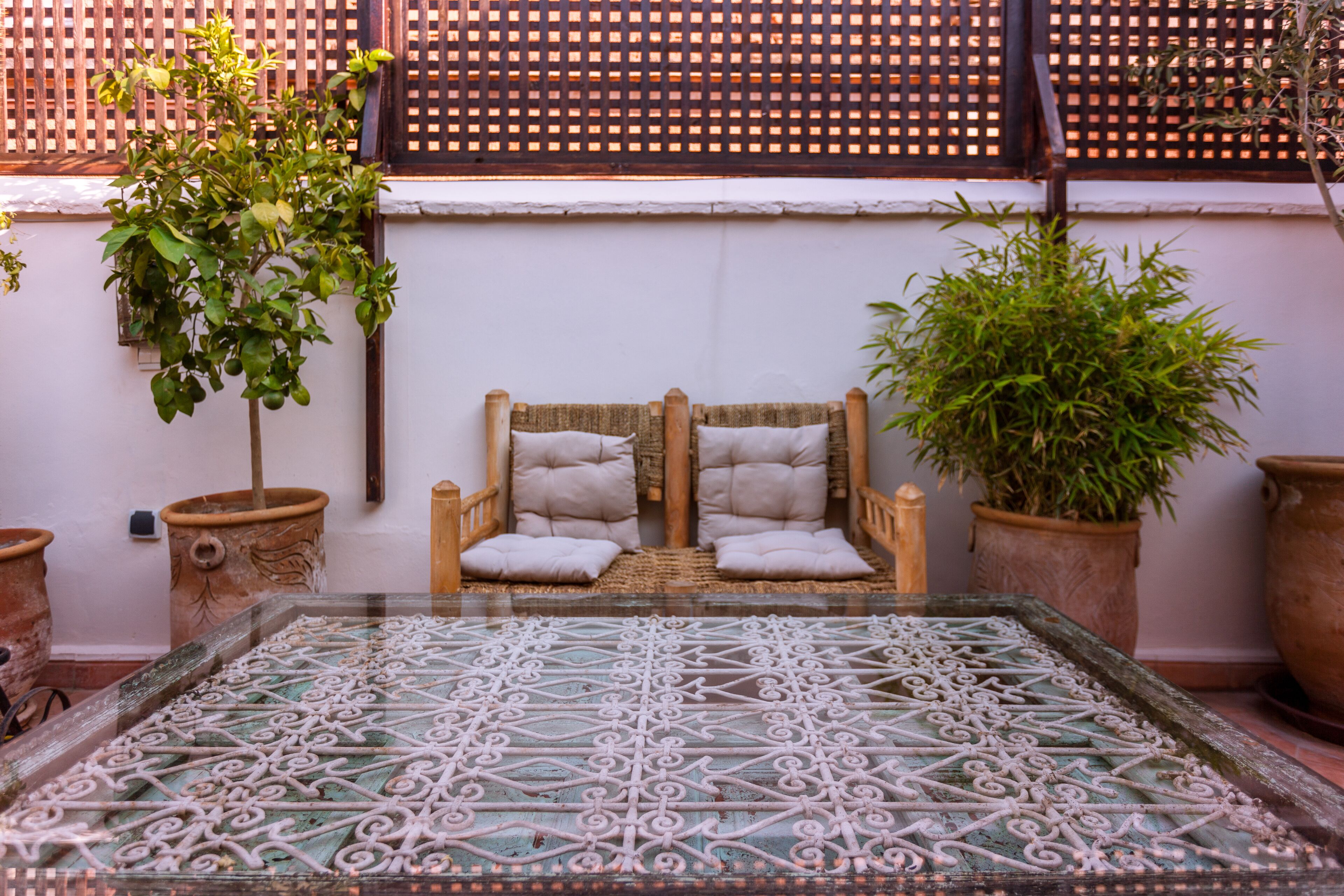 A traditional Moroccan-style seating area with a patterned floor, two cushioned chairs, and potted plants.