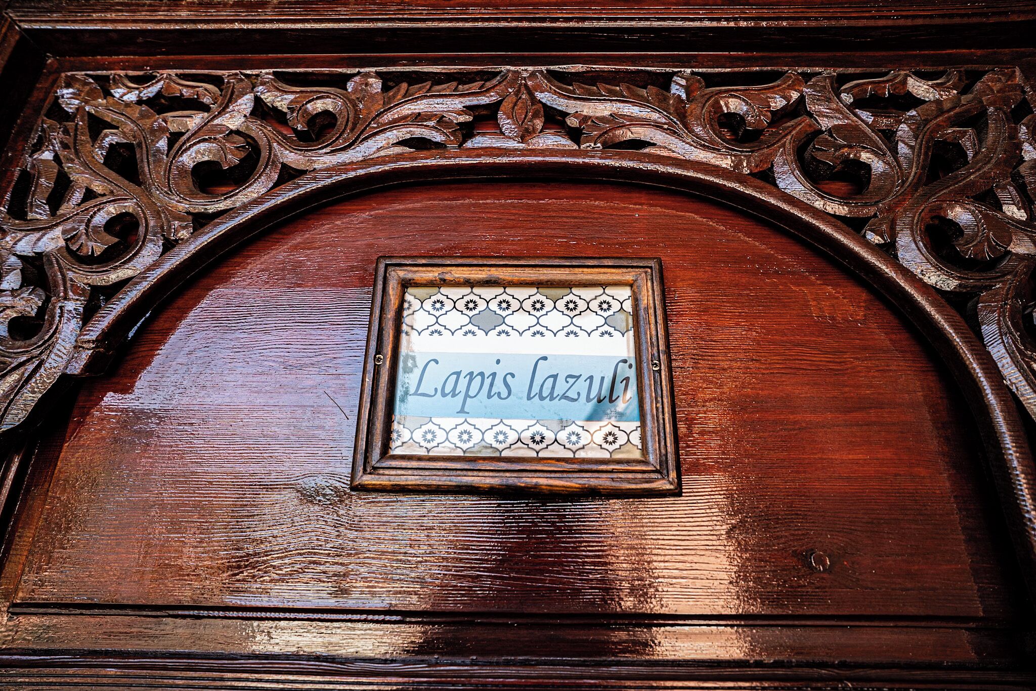 Una puerta de madera con un marco tallado ornamentado y un letrero que dice 'Lapis lazuli'.
