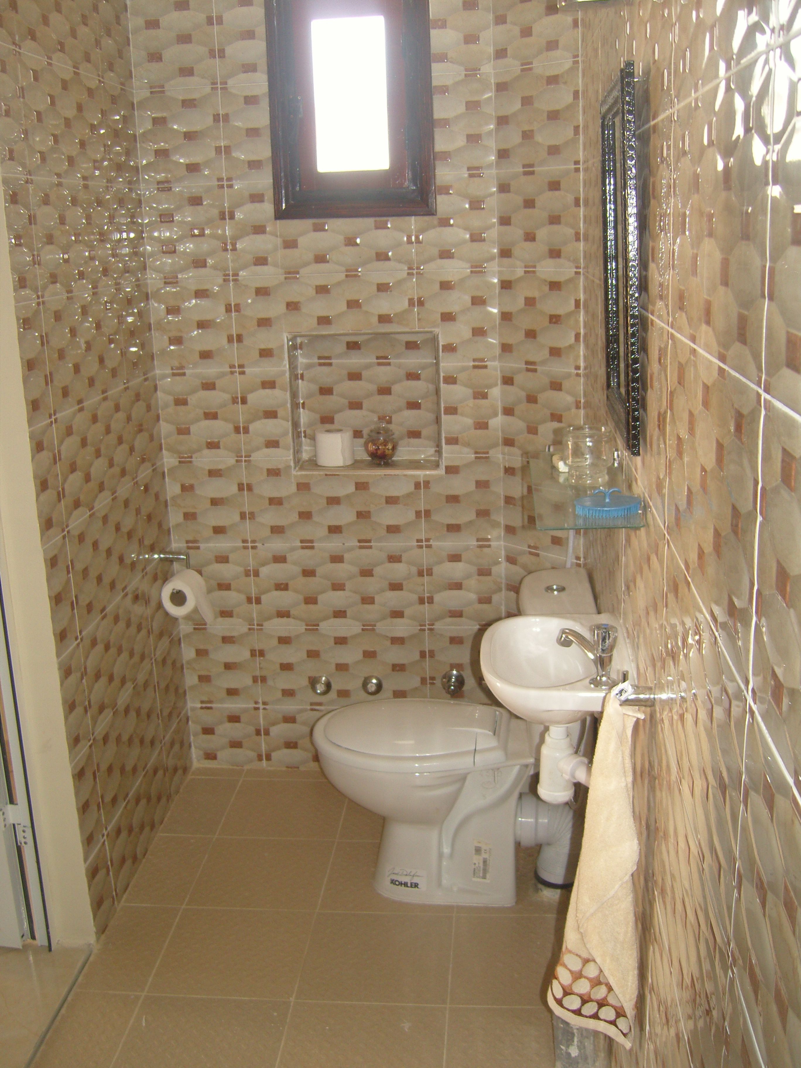 A bathroom with a toilet, sink, and mirror. There is a towel rack and a small shelf with toiletries.