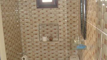 A bathroom with a toilet, sink, and mirror. There is a towel rack and a small shelf with toiletries.