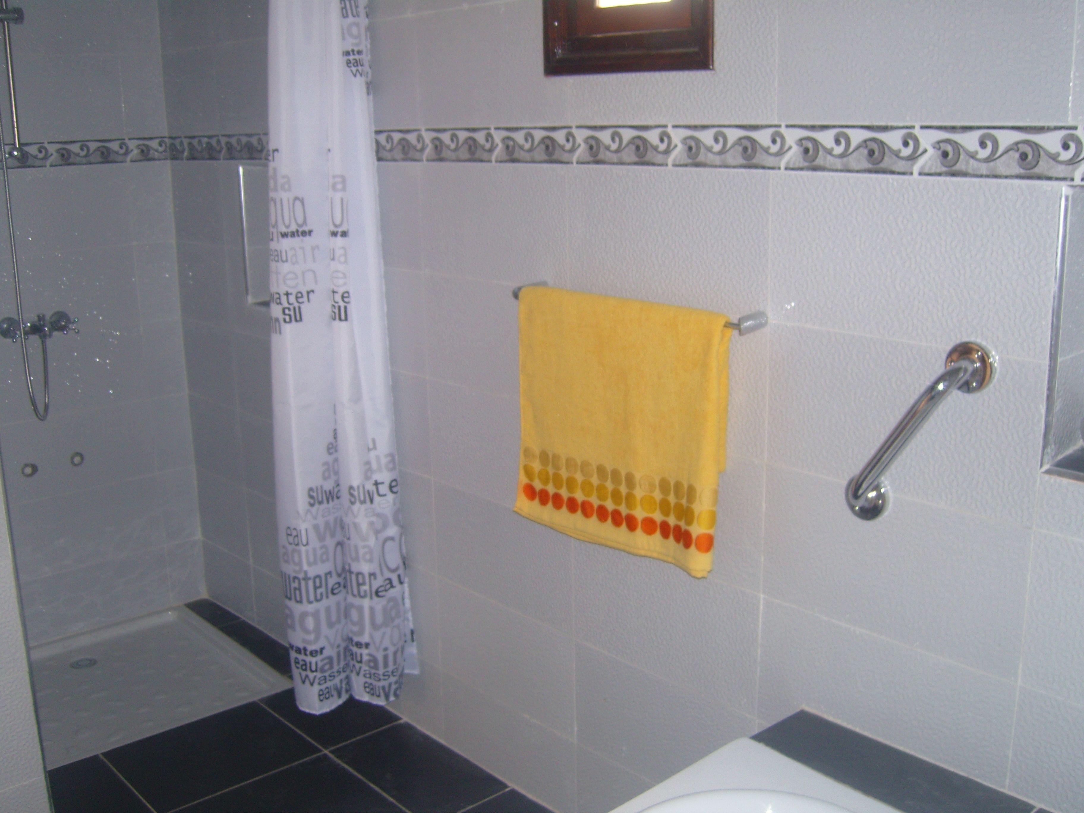 Un baño con ducha, un perchero y una toalla amarilla, además de una cortina de ducha con texto alusivo al agua.