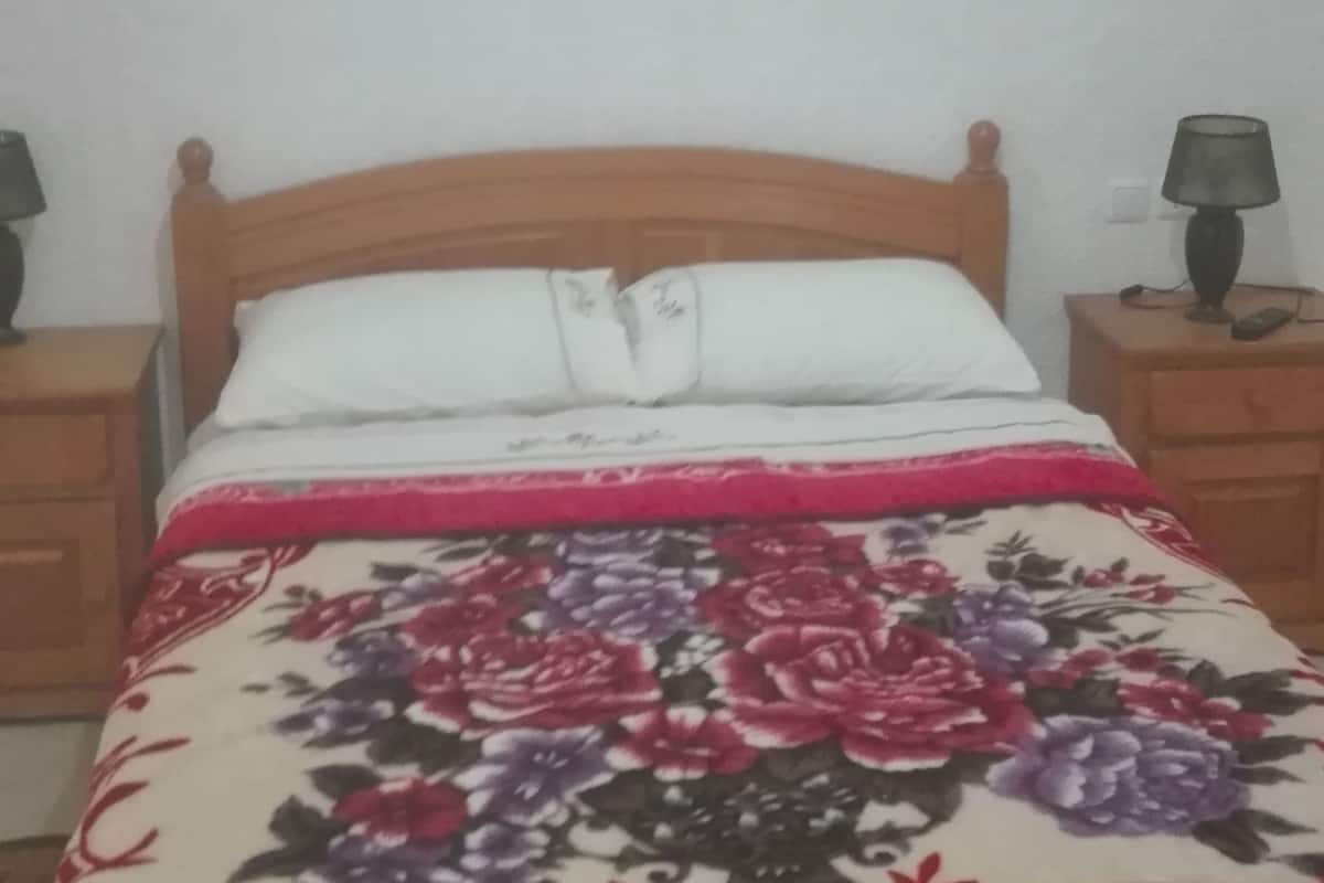 A bed with a floral bedspread, two bedside tables with lamps, and a framed floral artwork on the wall.
