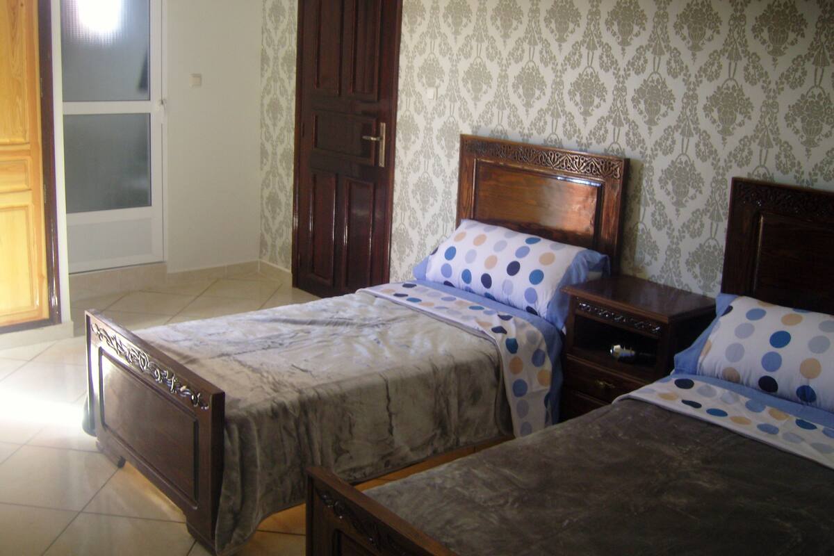 A bedroom with two beds, a wooden headboard, a nightstand, and a door.