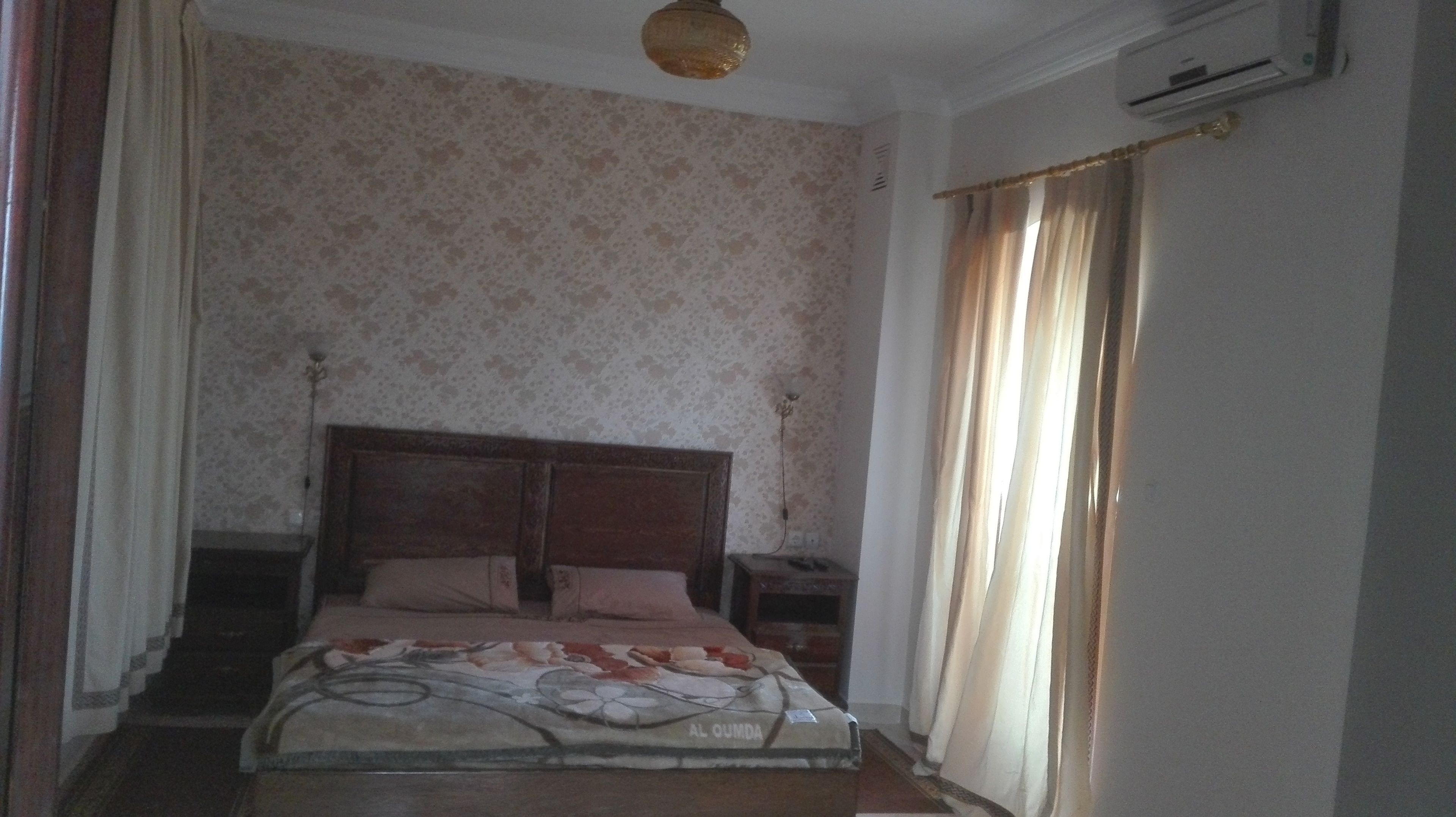 Un dormitorio con una cama, una mesita de noche, una lámpara y una ventana con cortinas.