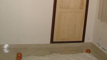 A room with a wooden wardrobe, a mounted television, and a tiled floor.