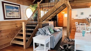 A wooden interior with a staircase, a sofa with patterned cushions, a small table, and a dining area with chairs. - Nautical Beach Properties (Hampton)