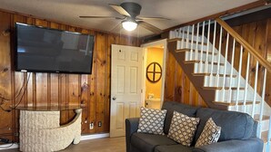 A living room with a flat-screen TV, a wooden wall, a staircase, and a gray sofa with patterned cushions. - Nautical Beach Properties (Hampton)