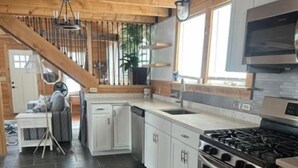 A modern kitchen with white cabinets, a stainless steel stove, and a large window. - Nautical Beach Properties (Hampton)