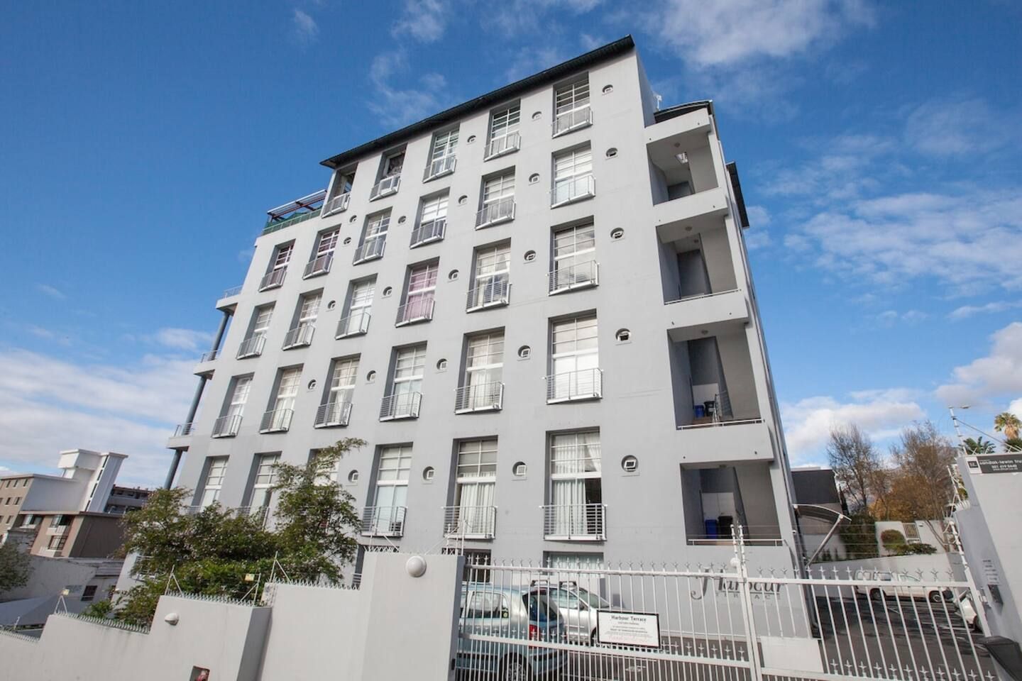 A multi-story residential building with balconies, a gated entrance, and a clear sky.
